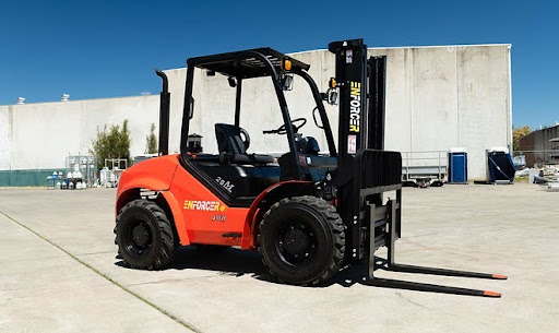 Red Enforcer forklift parked outdoors on a concrete surface near industrial buildings under a clear blue sky.